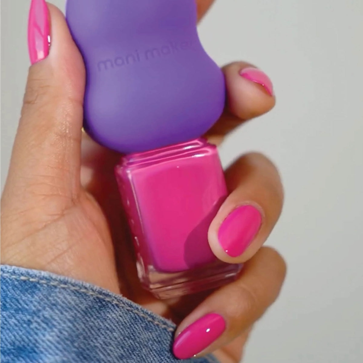 Hand with bright pink nails holding Dermelect Mani Maker base coat tool and matching pink polish bottle