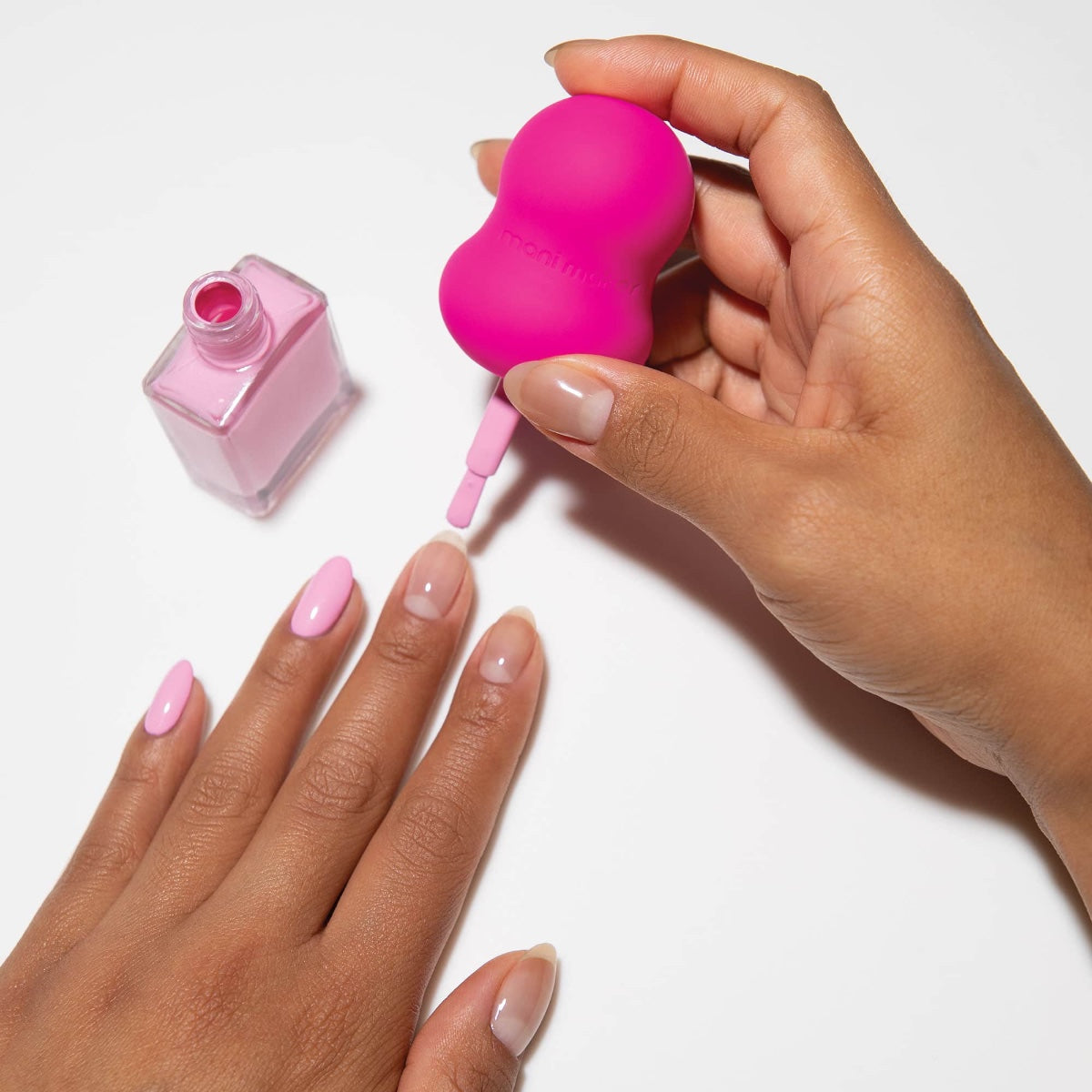Woman applying Dermelect Mani Maker base coat with pink brush and bottle for glossy salon quality nails