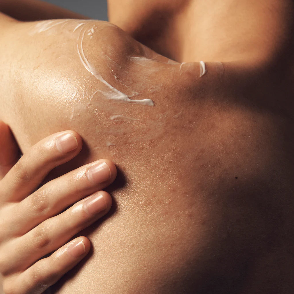 Close up of a person applying lavender firming body lotion on their shoulder for smooth skin