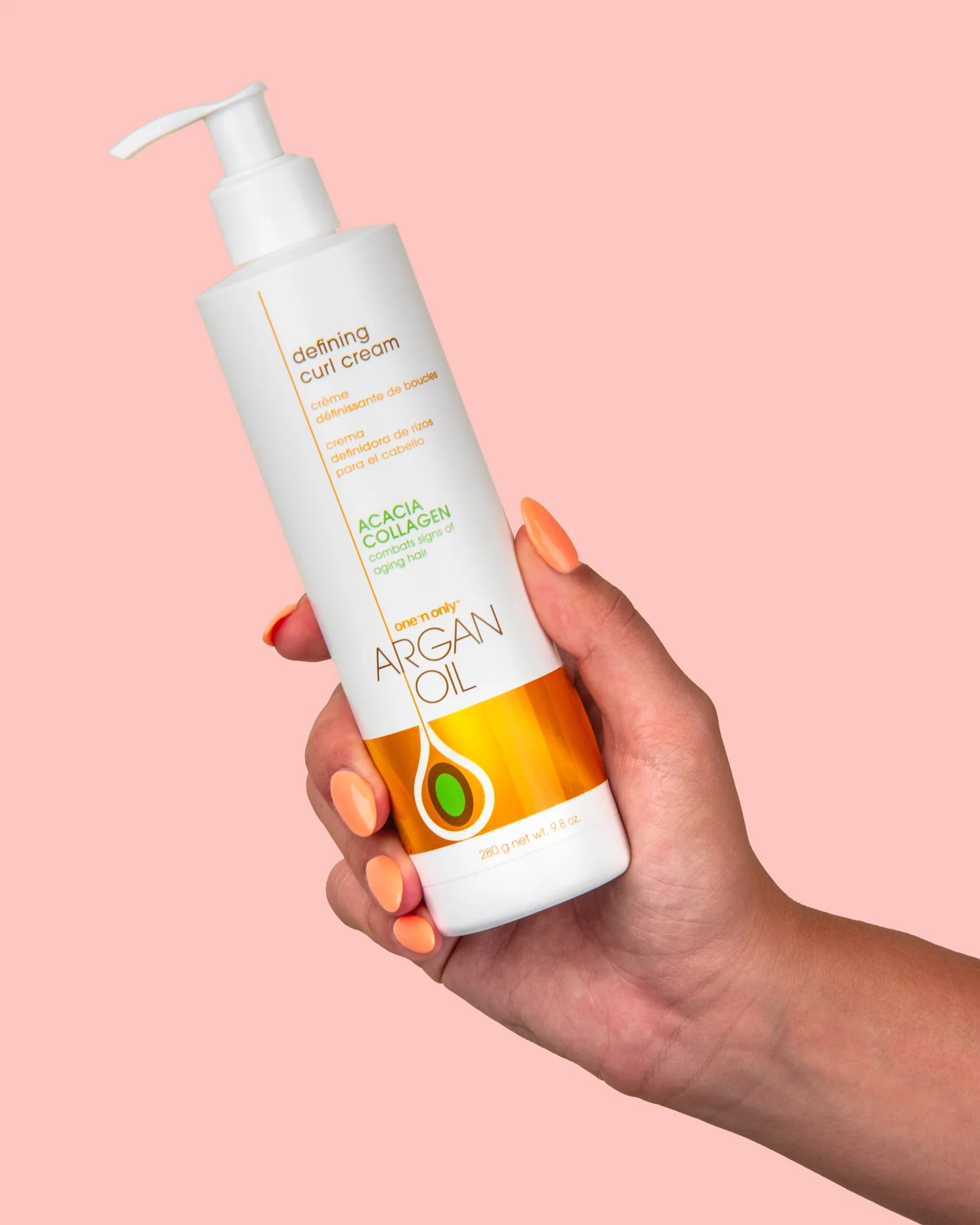 One N Only argan oil curl cream bottle held in hand with pink background