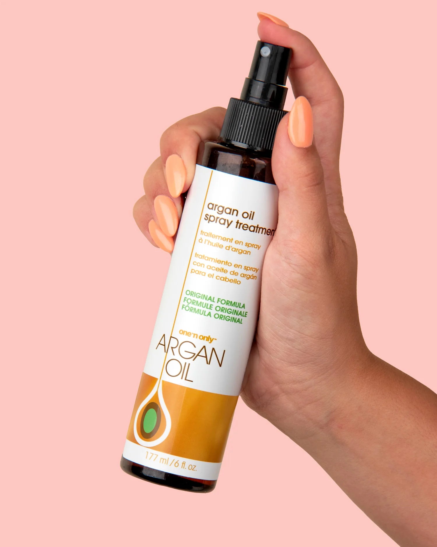 One N Only argan oil spray treatment bottle held in hand with peach nail polish on pink background