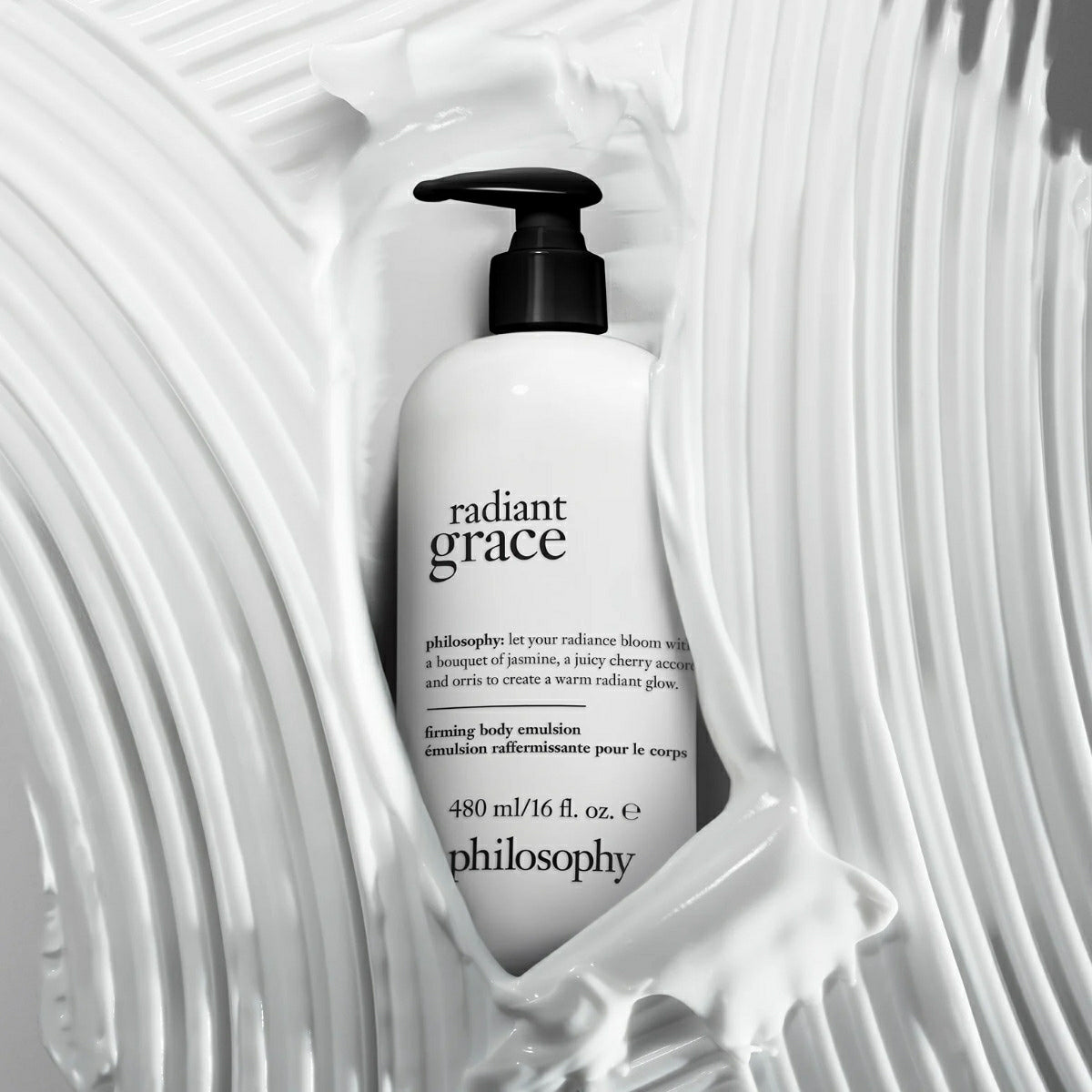 Philosophy Radiant Grace body emulsion bottle surrounded by creamy white lotion texture