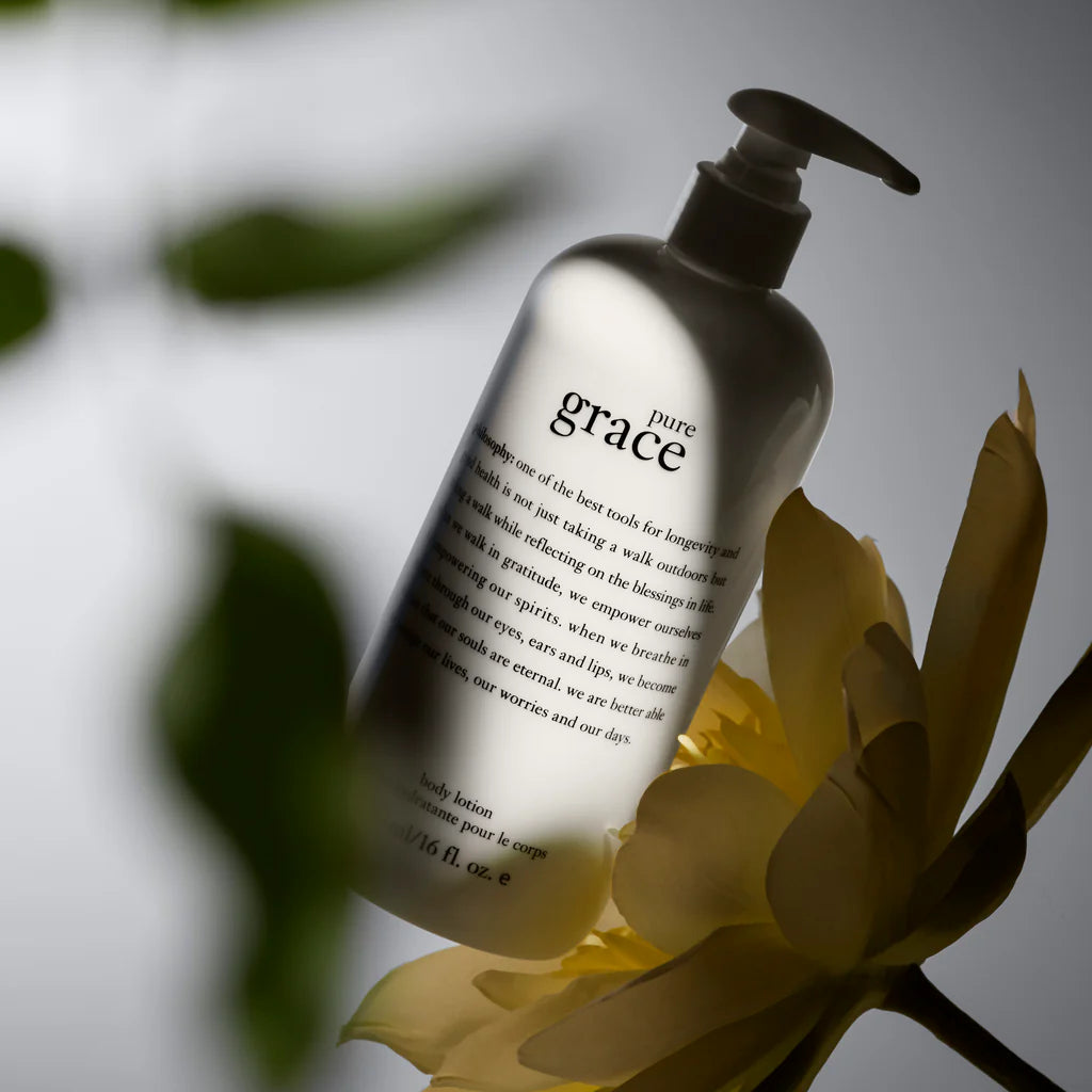 Philosophy Pure Grace lotion bottle with pump dispenser surrounded by soft natural light and flower petals