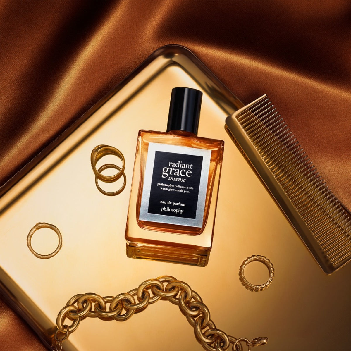 Philosophy Radiant Grace Intense eau de parfum bottle with gold rings, chain, and comb on golden tray