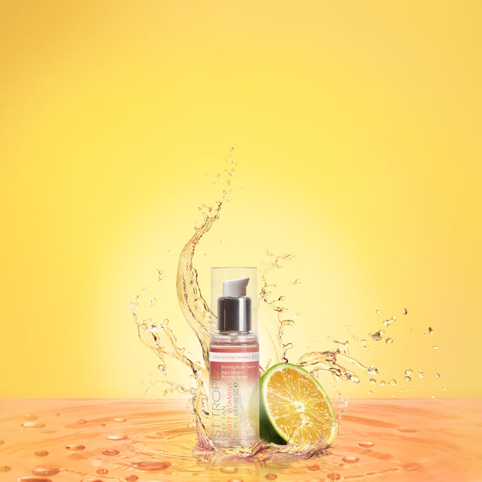 St Tropez self-tan bronzing water bottle with water splash and lime slice on yellow background