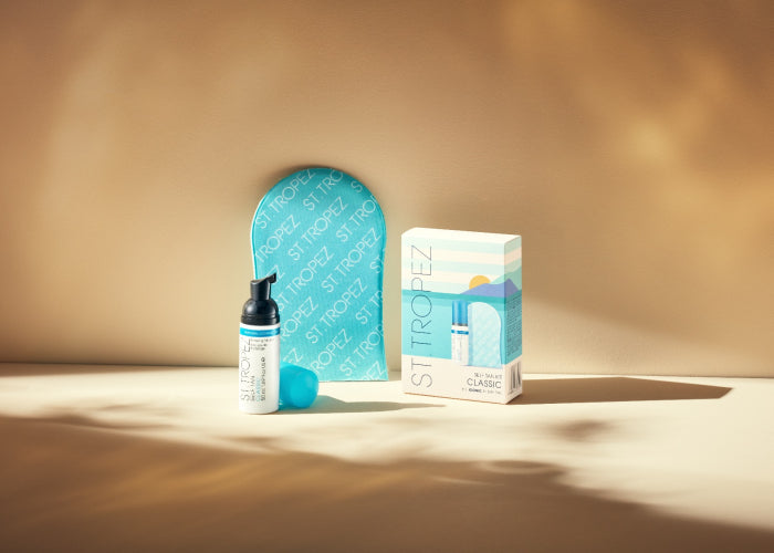 St. Tropez self tan kit with bronzing mousse, applicator mitt, and packaging on a beige surface