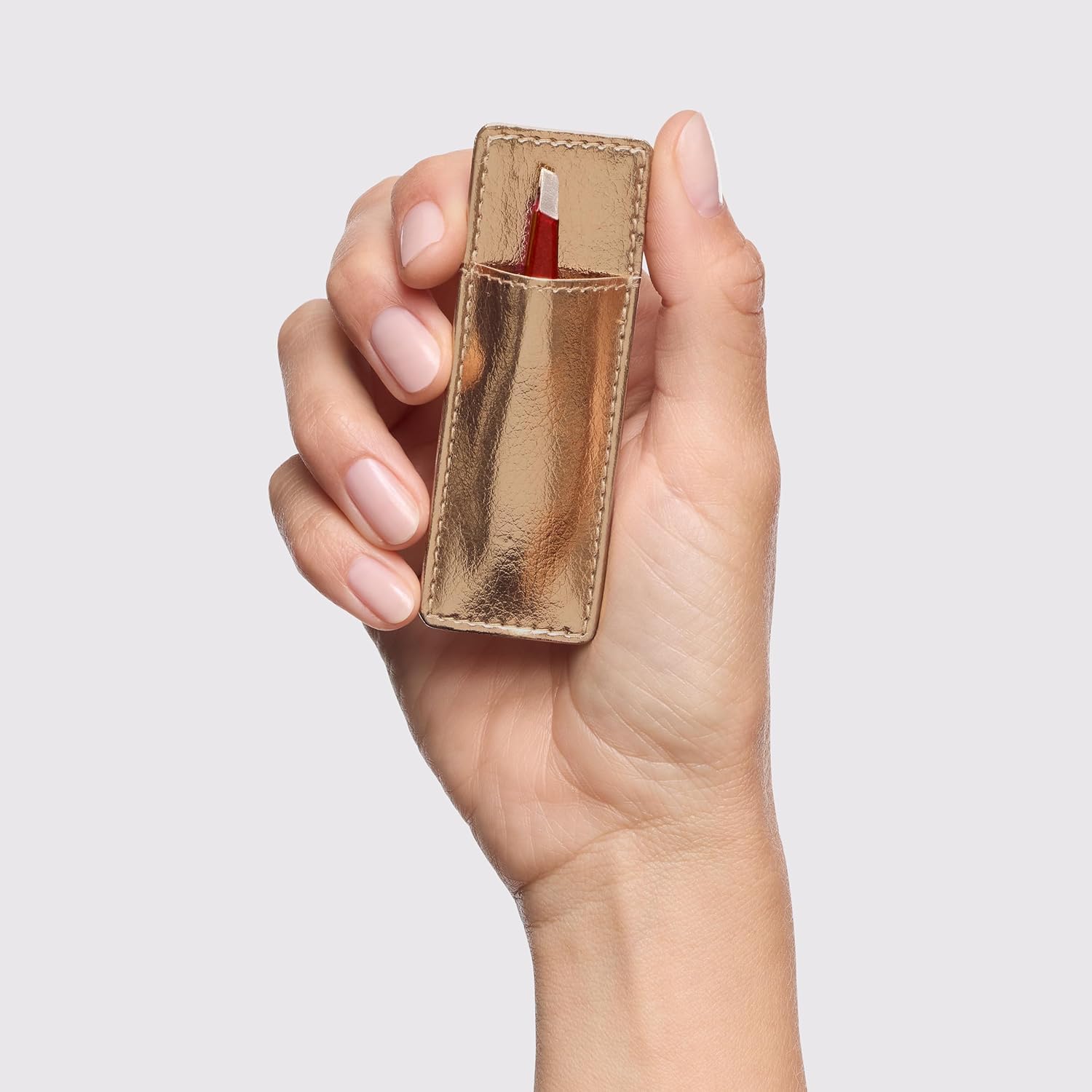 Hand holding Tweezerman mini slant tweezer in a stylish gold case for precise eyebrow shaping