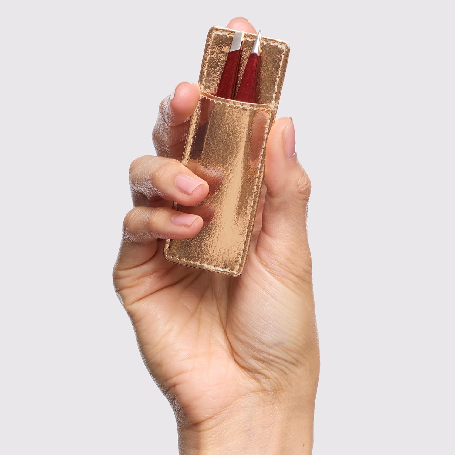 Tweezerman mini tweezer set in a gold case held in a hand for precise brow shaping