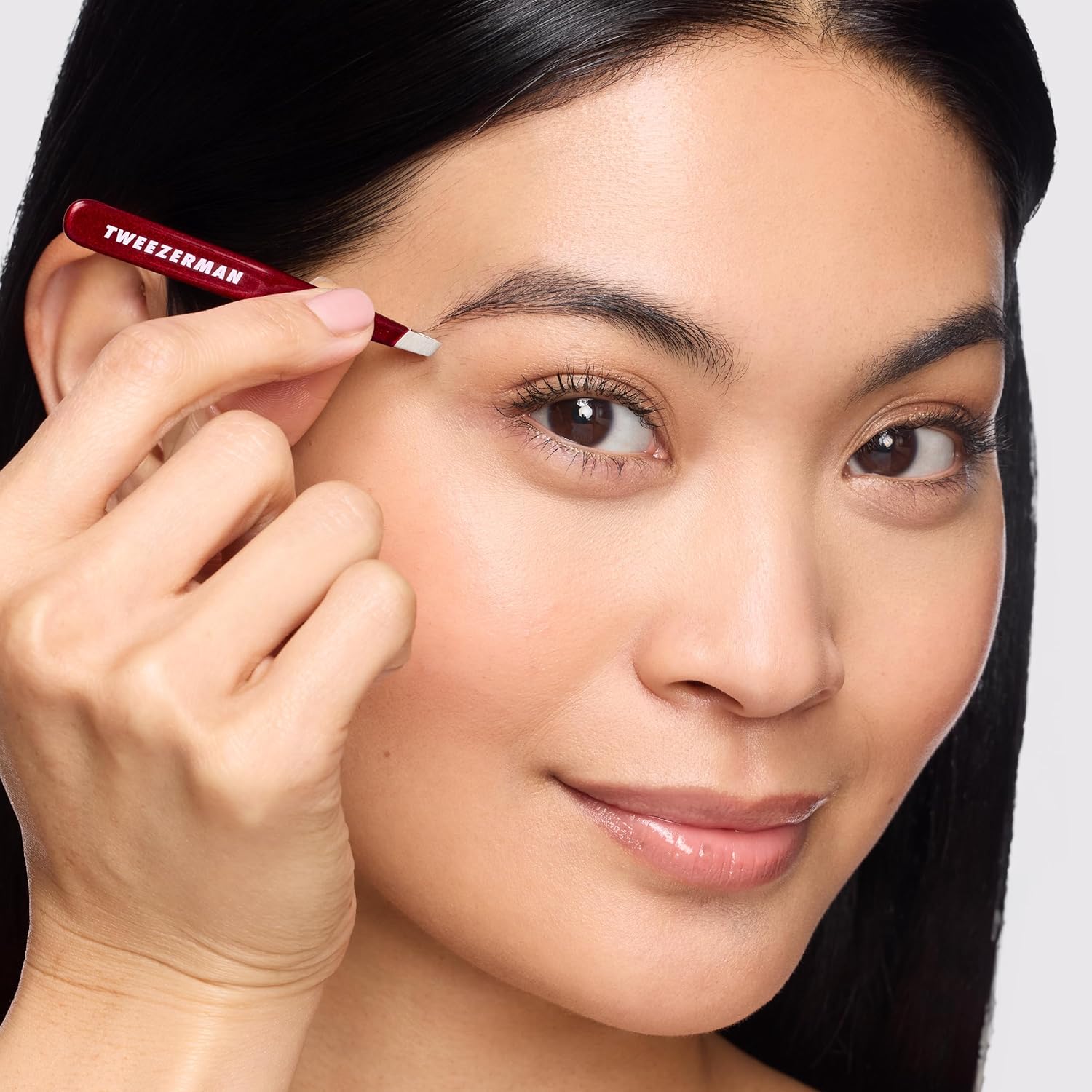 Tweezerman mini tweezer set being used for precise eyebrow grooming with a focused user