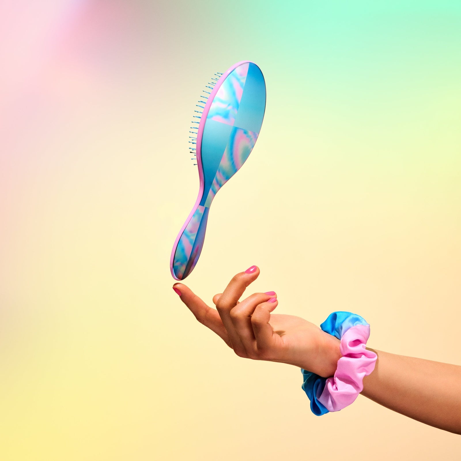 Wet Brush Galactic Waves bundle with blue and pink swirl hairbrush held by hand wearing matching scrunchies