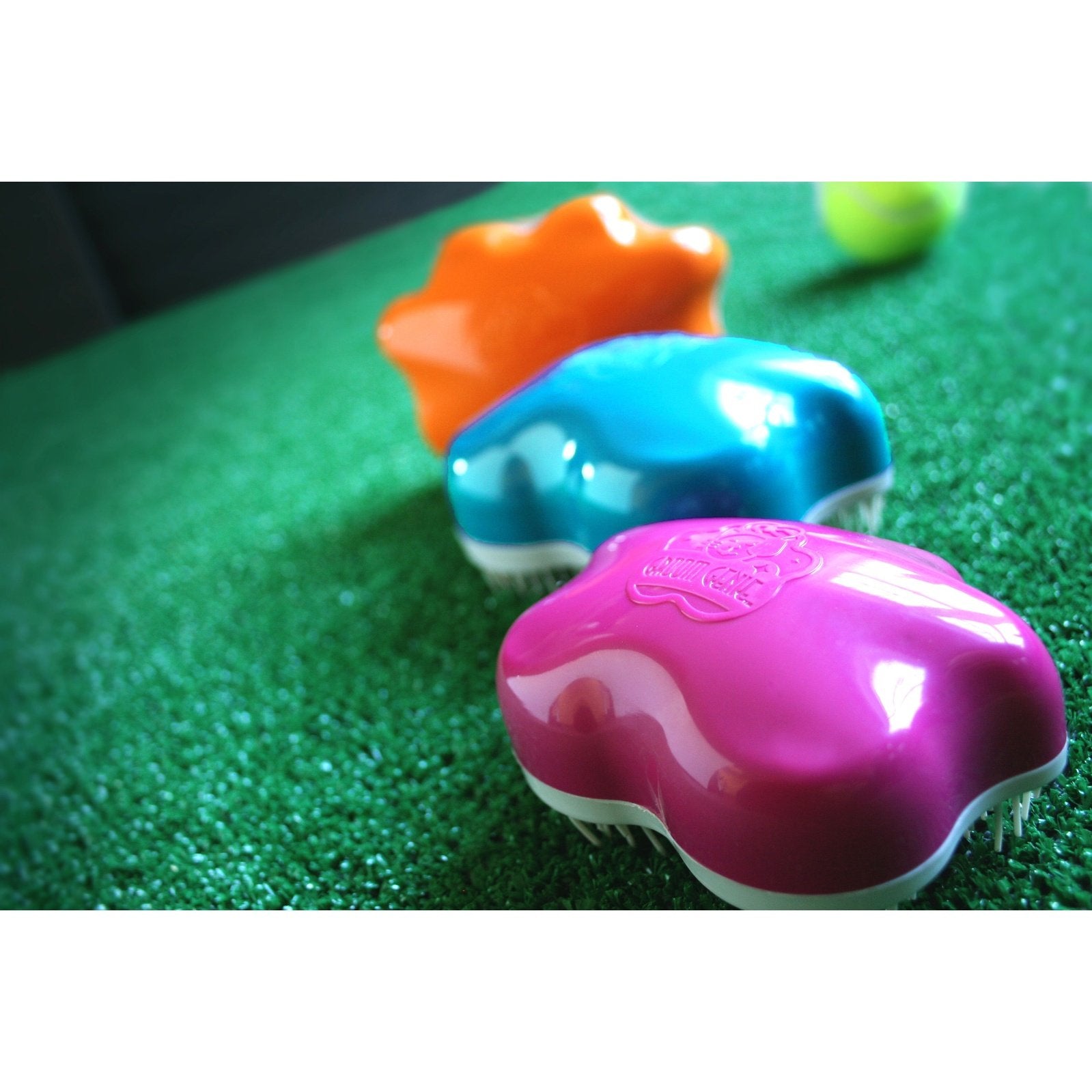 Colorful Groom Genie Teeny pet brush in pink blue and orange with soft bristles on green surface