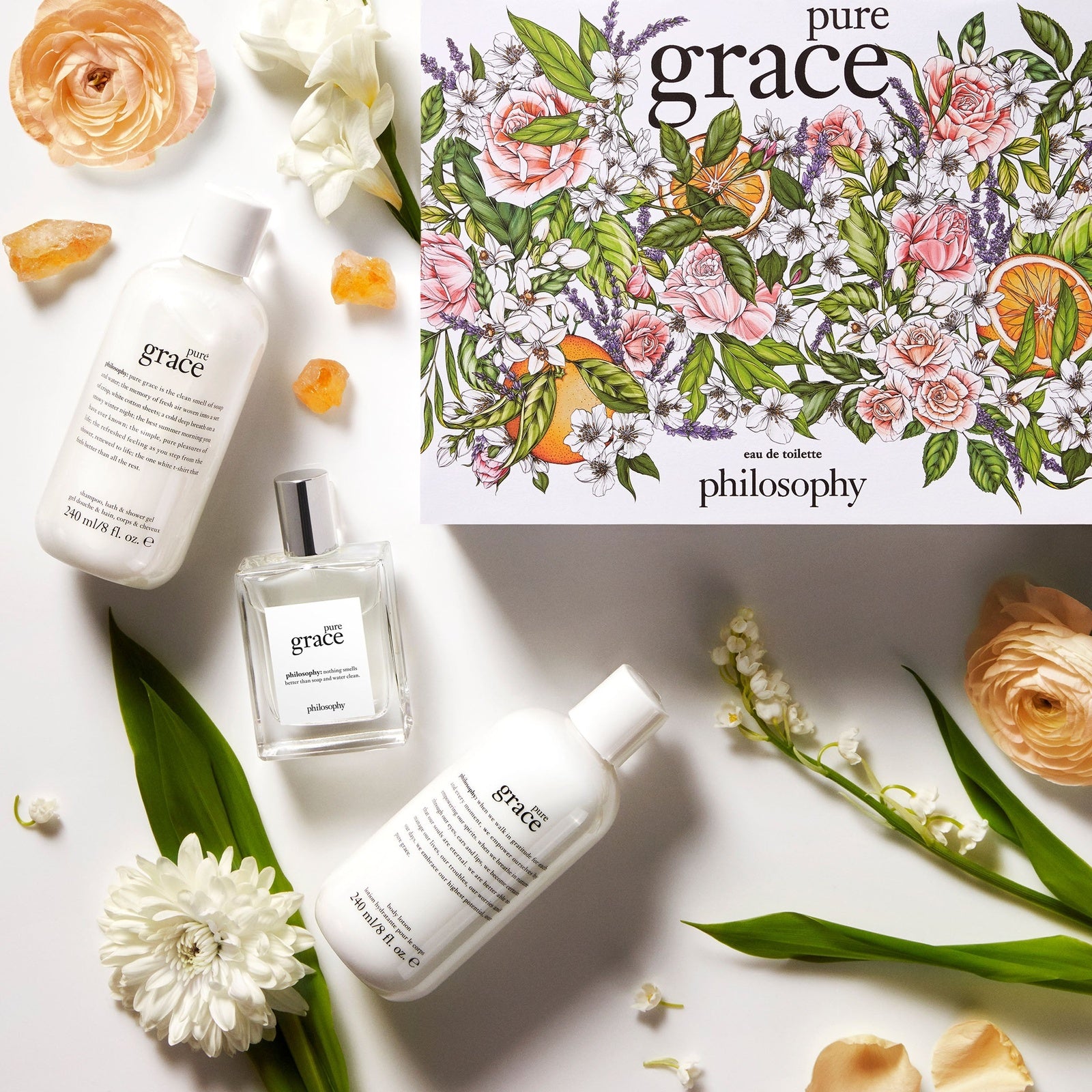 Philosophy Pure Grace gift set with floral illustrated box, eau de toilette, and moisturizing lotions surrounded by flowers