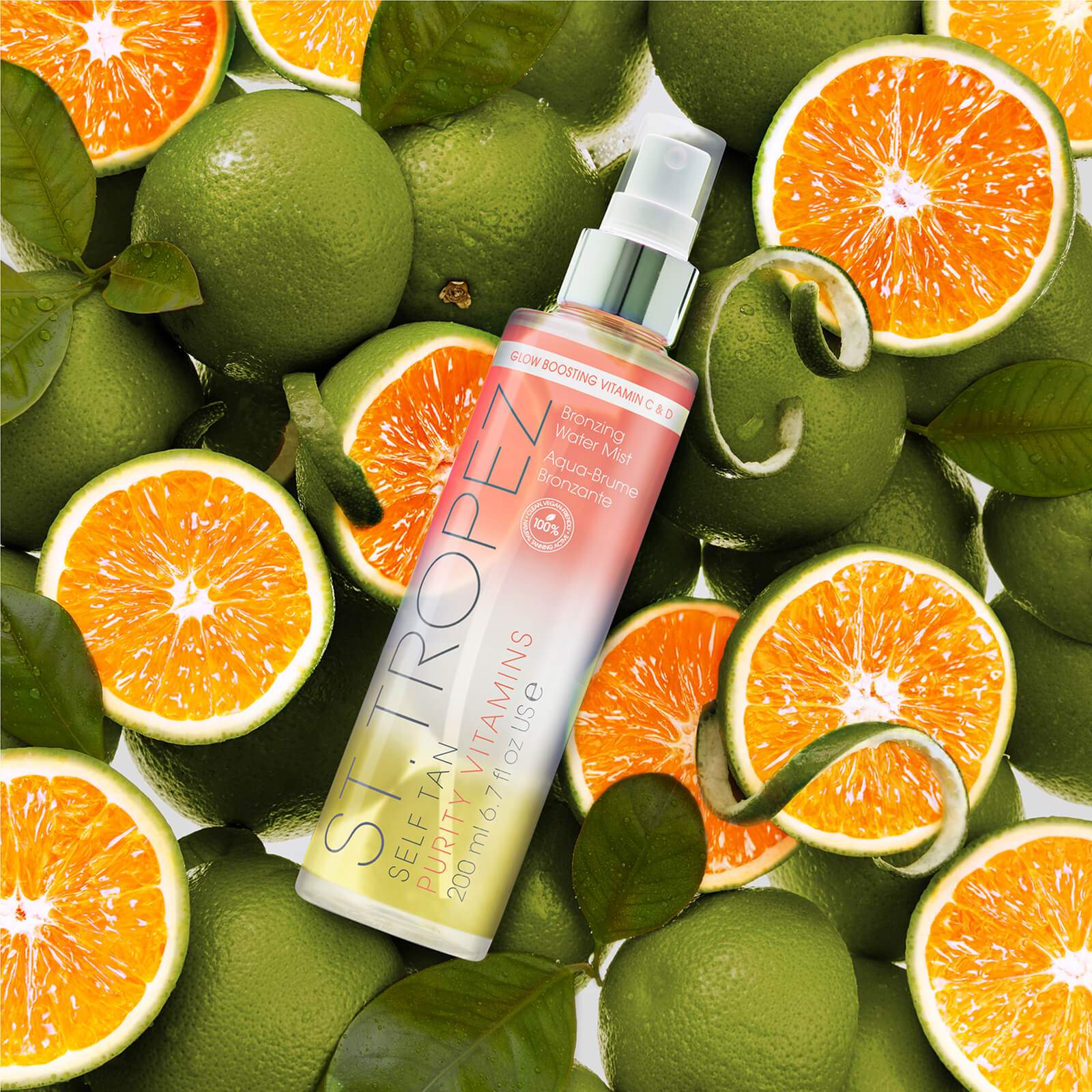 St Tropez bronzing water mist for glowing skin with vitamin C surrounded by fresh green and orange citrus fruits