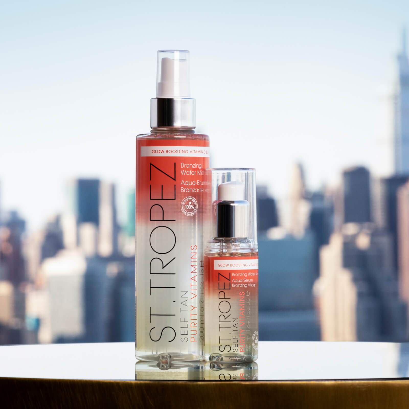 St Tropez bronzing water mist for glowing skin in two spray bottles with city skyline background