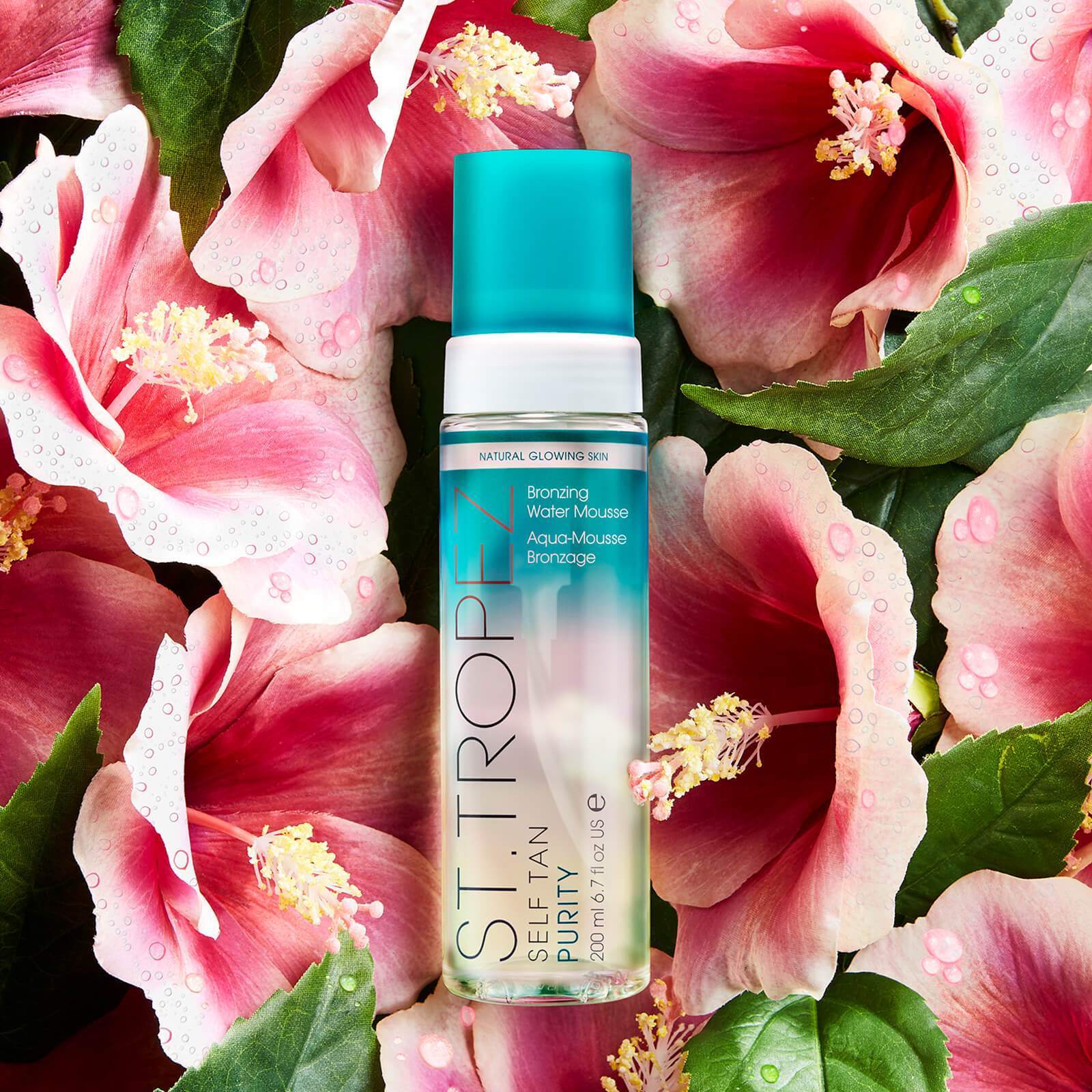 St Tropez Purity Bronzing Water Gel bottle surrounded by pink hibiscus flowers and green leaves