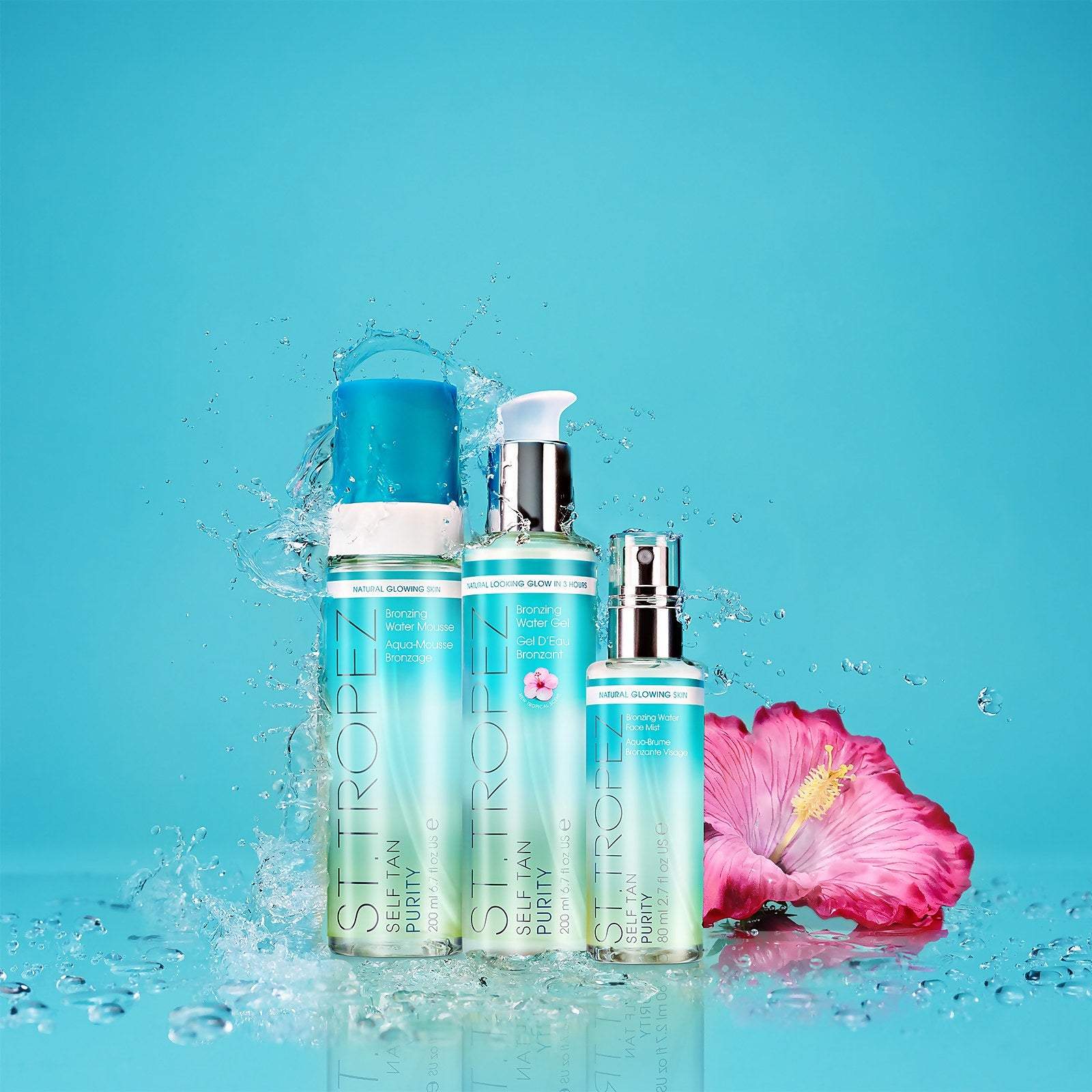 St Tropez self tanning mousse bottles with water splash and pink hibiscus flower on blue background