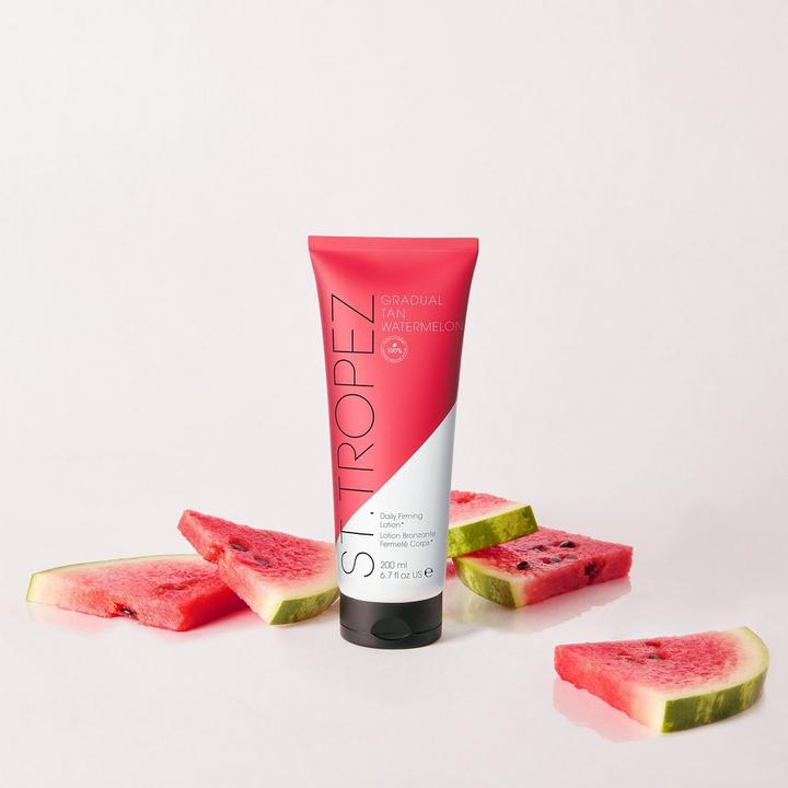 St Tropez watermelon self tanning lotion in pink and white tube surrounded by fresh watermelon slices
