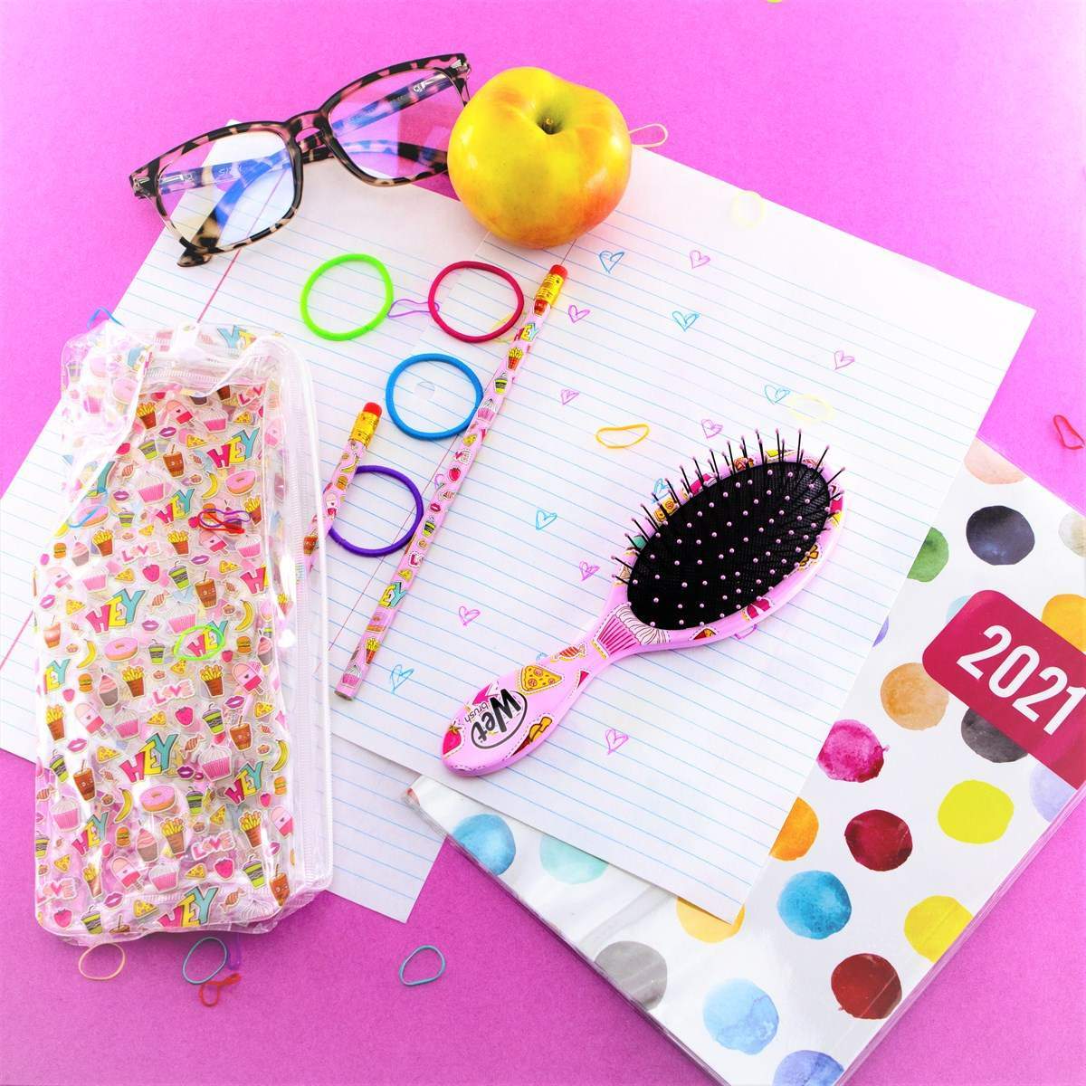 Wet Brush Back to School Detangling Brush Set with pink brush, colorful notebook, pencils, apple, and glasses on pink background
