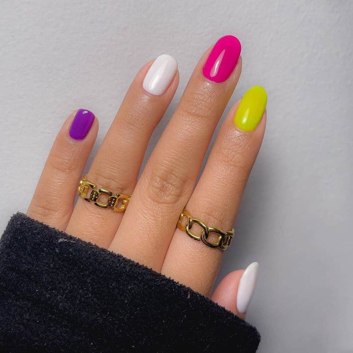 Hand with neon pink purple yellow and white almond nails wearing gold chain rings Dermelect Mani Maker base coat