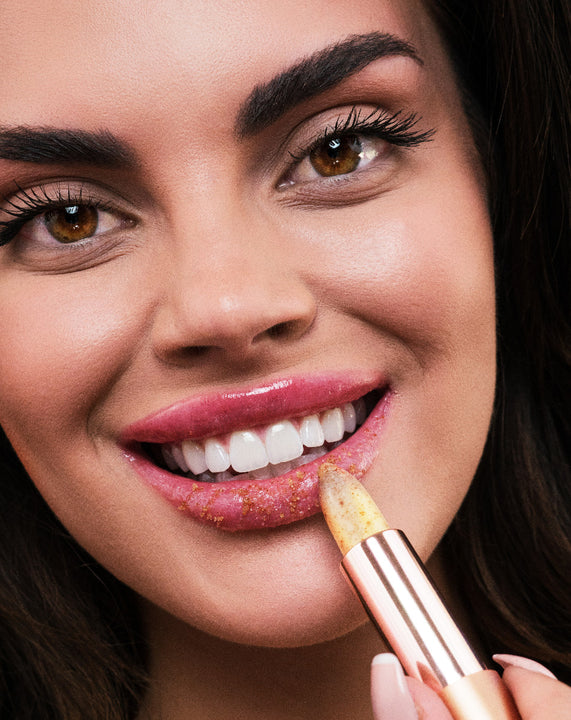 Karen Murrell woman applying natural lip scrub stick to her smiling lips with visible exfoliating sugar
