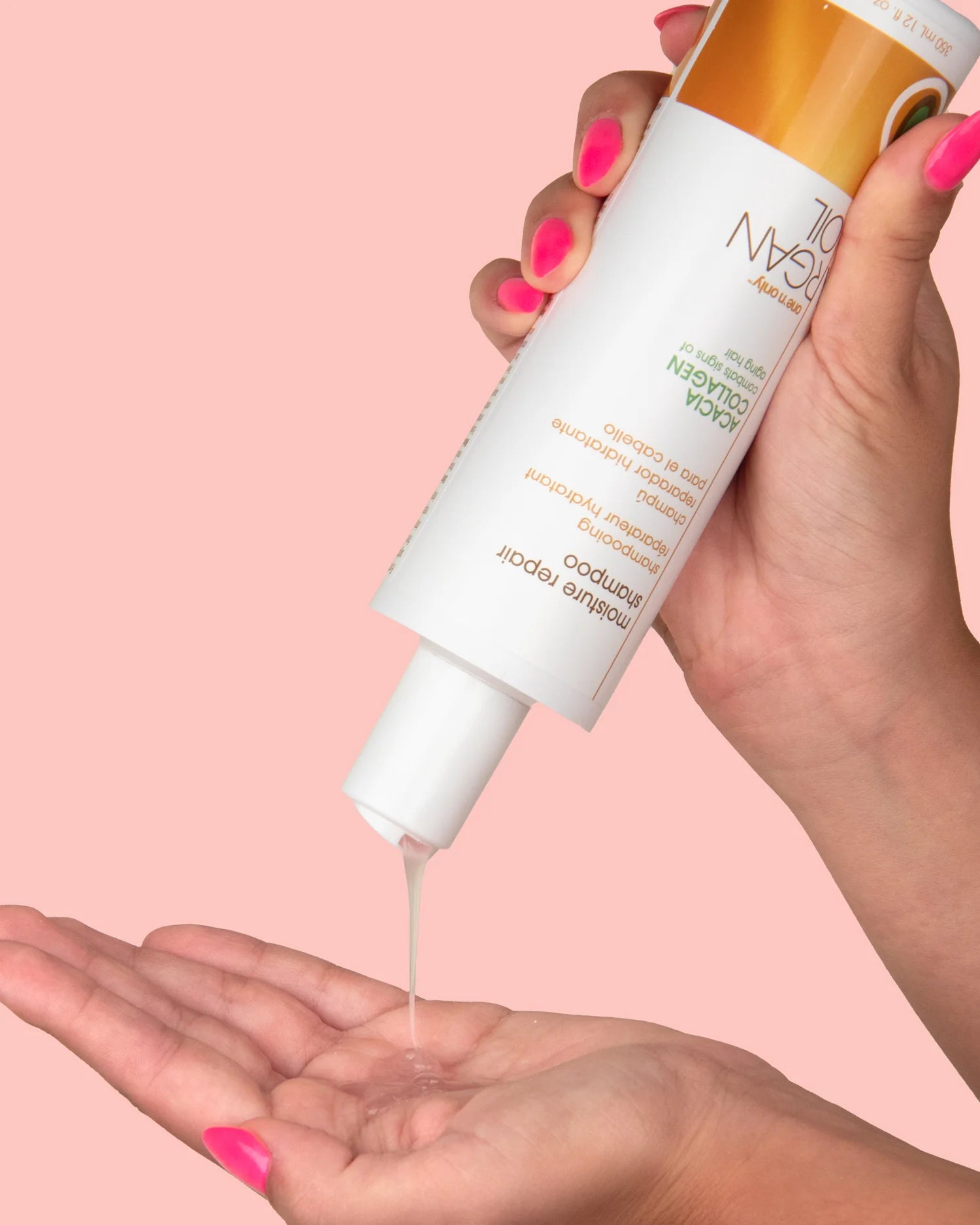 One N Only moisture repair shampoo being poured from bottle into a hand with pink background