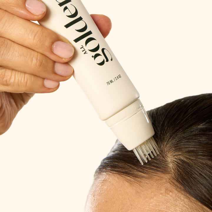 Hand applying All Golden Root Changer 1.8 oz to dark hair roots with precision applicator comb