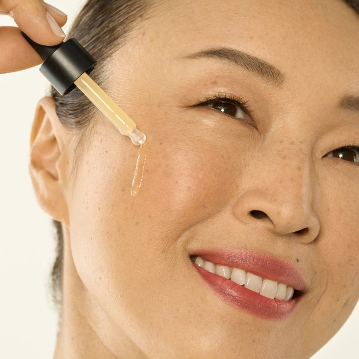 Woman applying firming face serum with peptides from All Golden using a dropper on her cheek