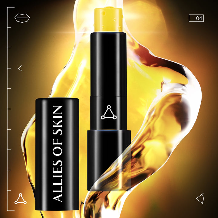 Black tube of Allies of Skin lip repair balm with yellow balm stick and glossy golden oil background