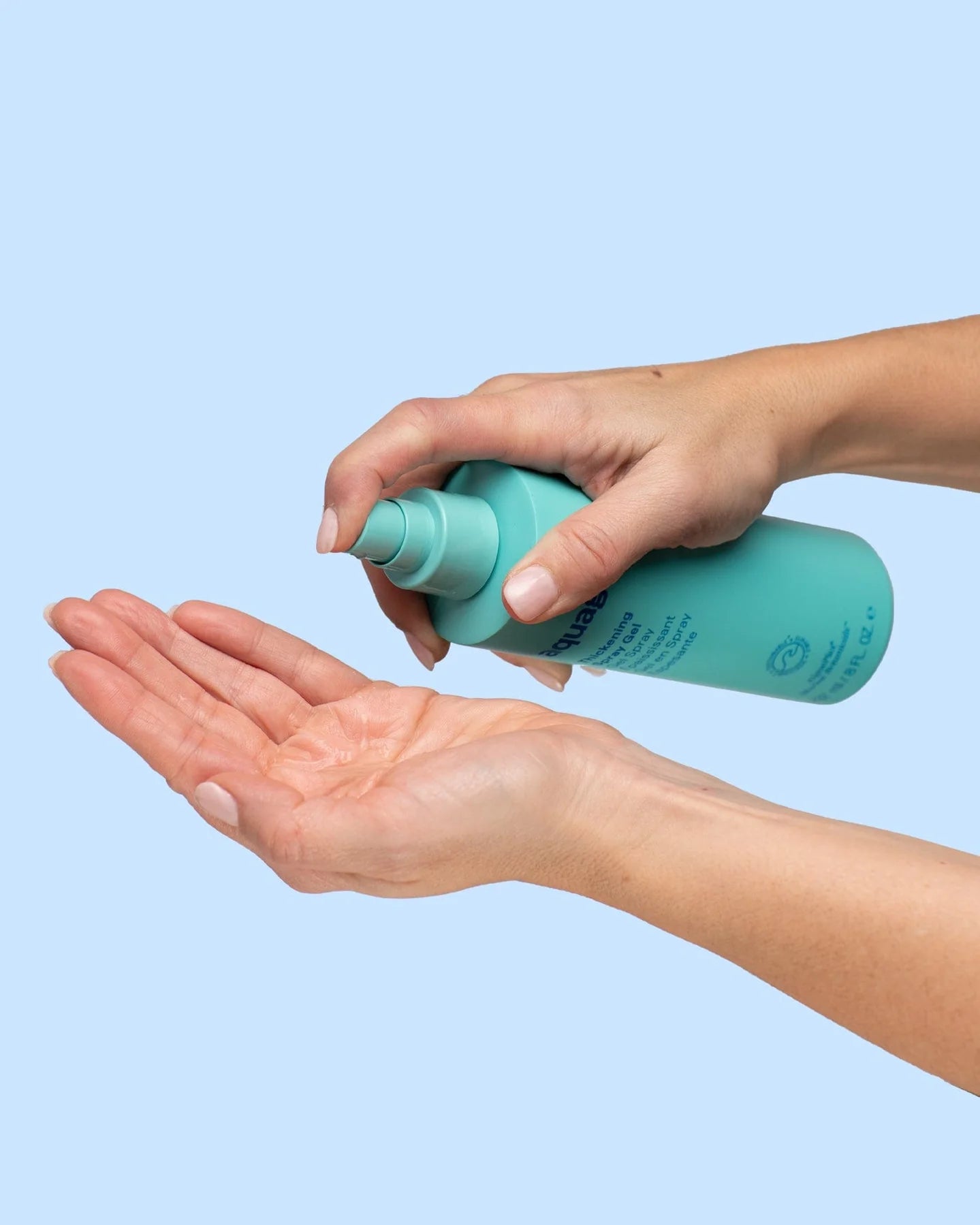 Person dispensing Aquage thickening spray gel from turquoise bottle onto palm against light blue background