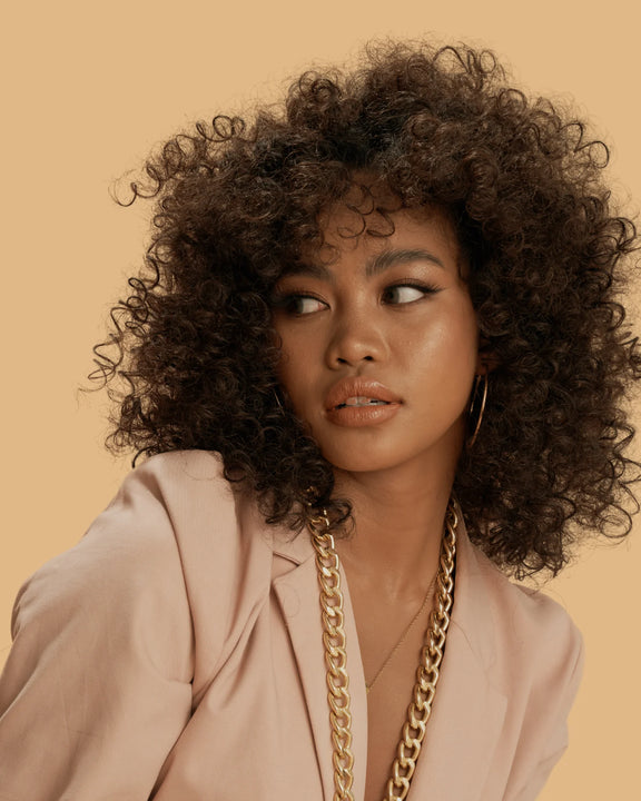 Woman with voluminous curly hair styled using One N Only argan oil curl cream wearing a beige blazer