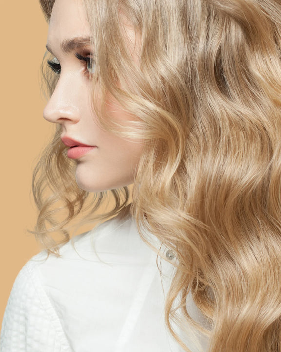 Blonde woman with shiny wavy hair showcasing smooth results of argan oil spray treatment