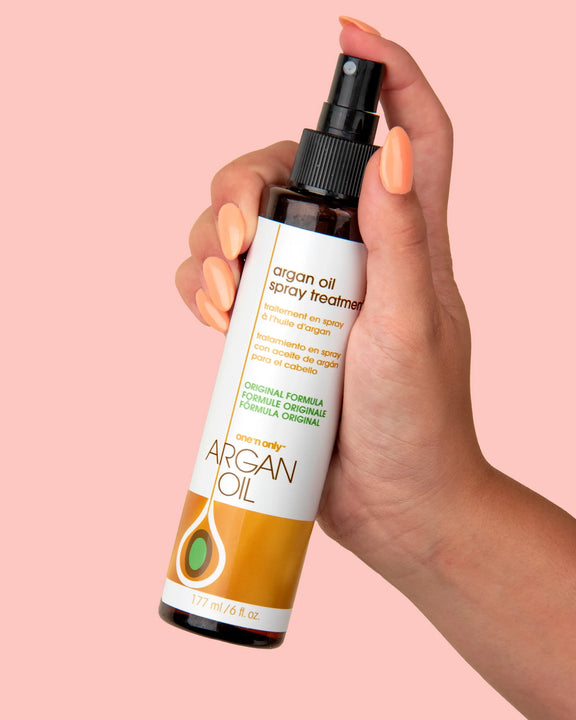One N Only argan oil spray treatment bottle held in hand with peach nail polish on pink background