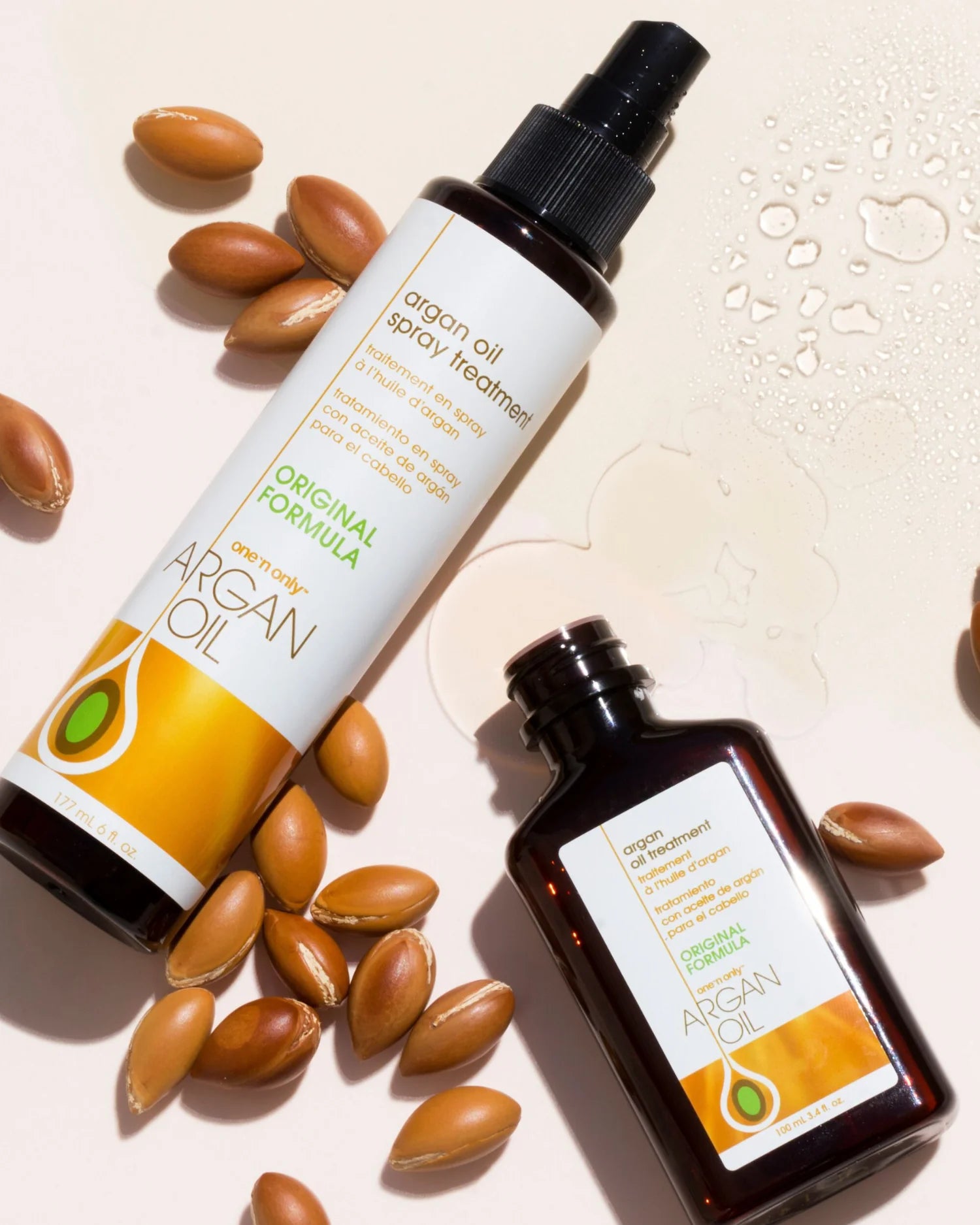 One N Only argan oil spray treatment bottles with argan nuts and oil drops on a light background