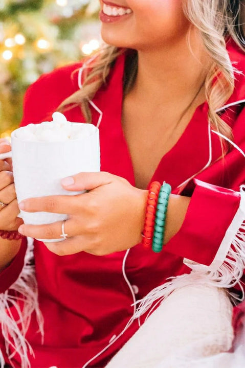 Teleties Christmas hair ties in red and green worn by a woman holding a mug of hot cocoa