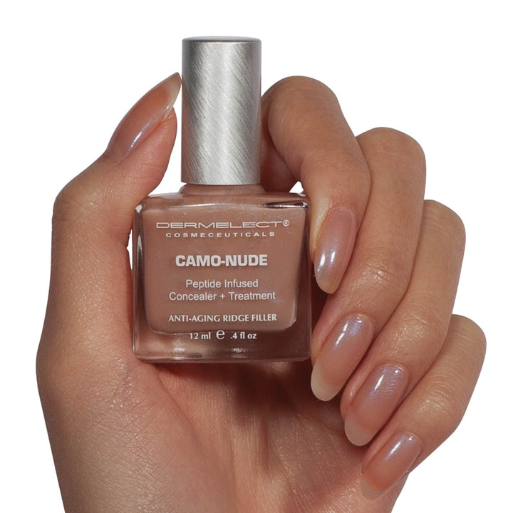 Hand holding Dermelect Camo-Nude ridge filler bottle showing nude concealer treatment and glossy natural nails