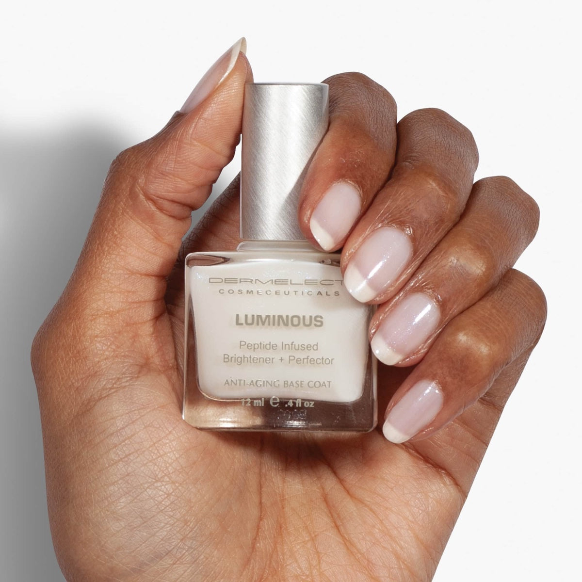 Dermelect Luminous Brightener review Hand with French manicure holding Dermelect Luminous bottle