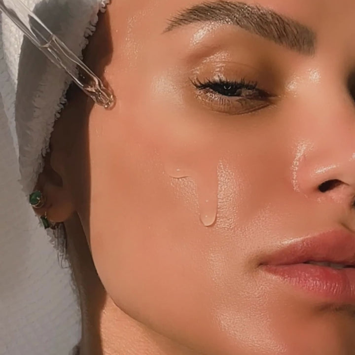 Close up of woman applying Dermelect Rapid Repair Serum with dropper on glowing dewy cheek and towel wrap
