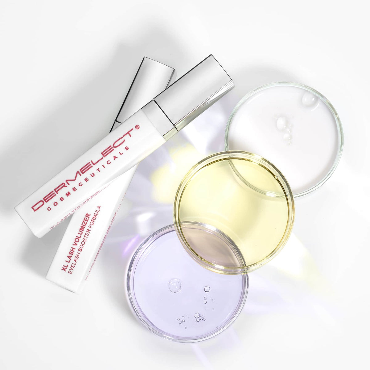 Dermelect XL Lash Volumizer white serum tubes with red logo beside three petri dishes holding clear yellow and purple gels