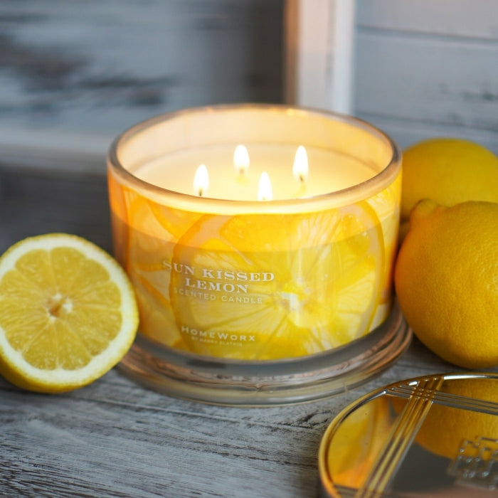 HomeWorx by Slatkin lemon scented candle with four wicks lit next to fresh lemons on wooden surface
