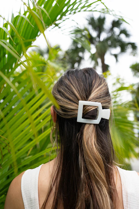 Medium white hair claw clip holding back a woman's hair among lush green foliage