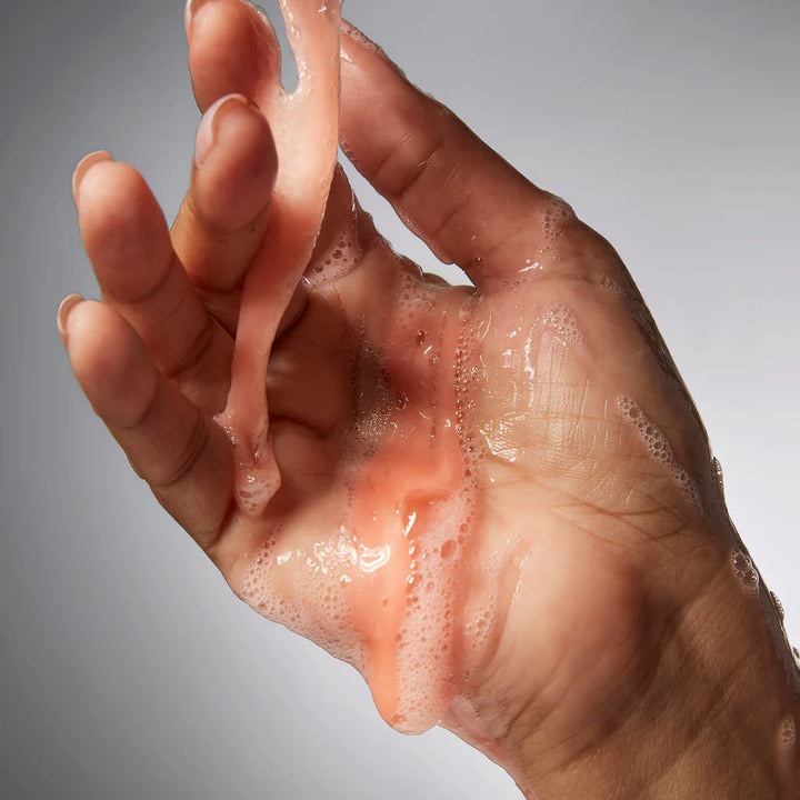 Hand covered in light pink foam from philosophy amazing grace shower gel dripping and spreading on skin