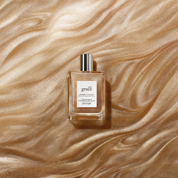 Philosophy Pure Grace body oil in a clear glass bottle with silver cap on shimmering gold fabric