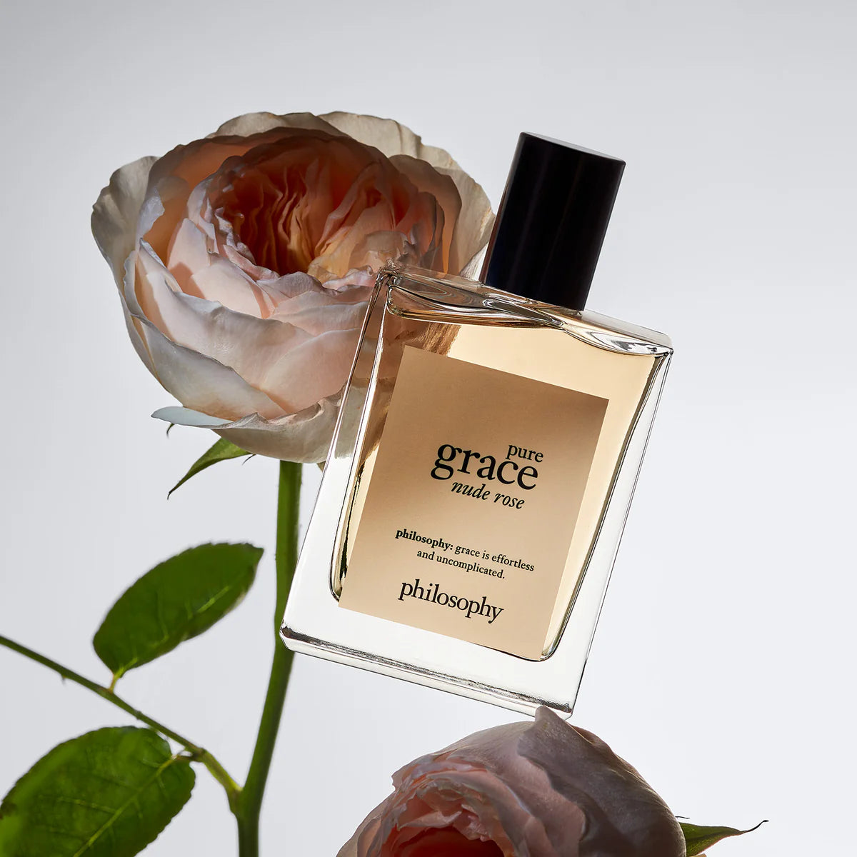 Philosophy Pure Grace Nude Rose perfume bottle next to soft pink and peach rose flowers