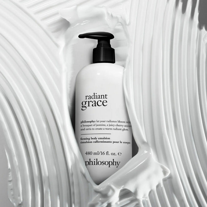 Philosophy Radiant Grace body emulsion bottle surrounded by creamy white lotion texture