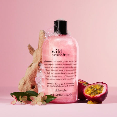 Philosophy shower gel 16 oz wild passionfruit scent with bubbles, placed next to passionfruit and wood on pink background