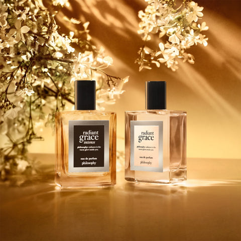 Two bottles of Philosophy Radiant Grace Intense eau de parfum with floral background and warm lighting