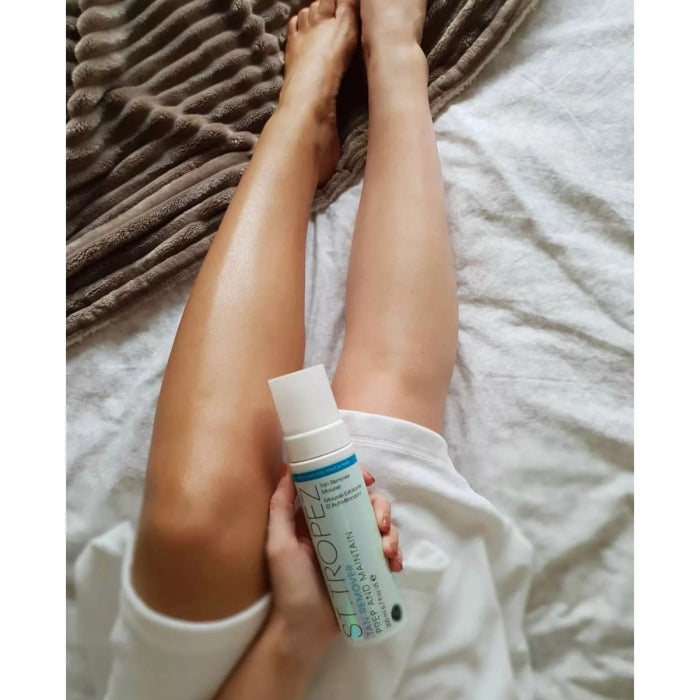 St. Tropez tan remover mousse with one leg showing a tan and the other leg clear on a white blanket