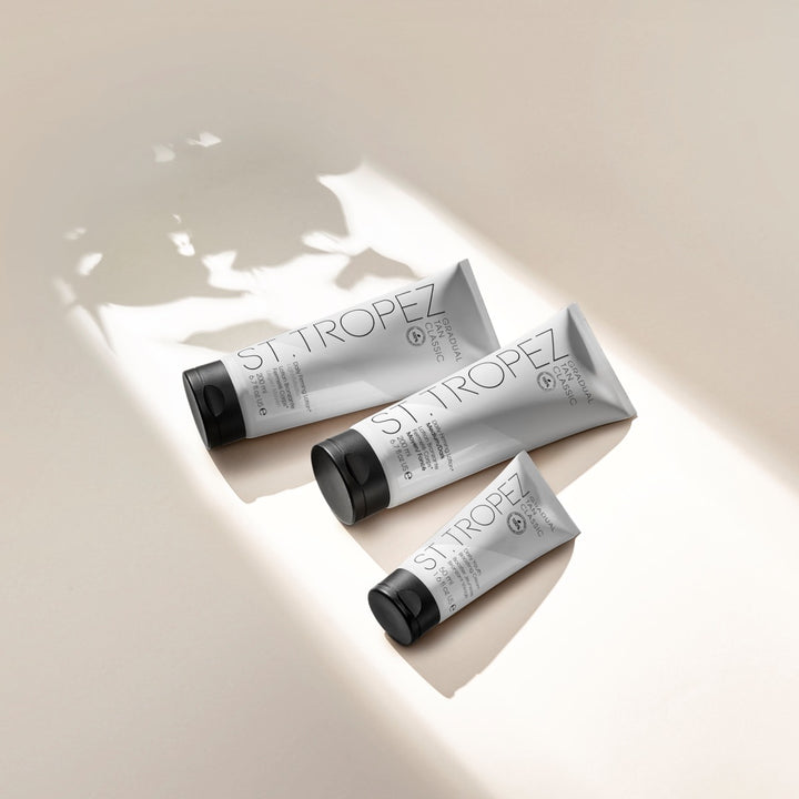 St Tropez light medium tan lotion in three silver tubes with black caps on beige background