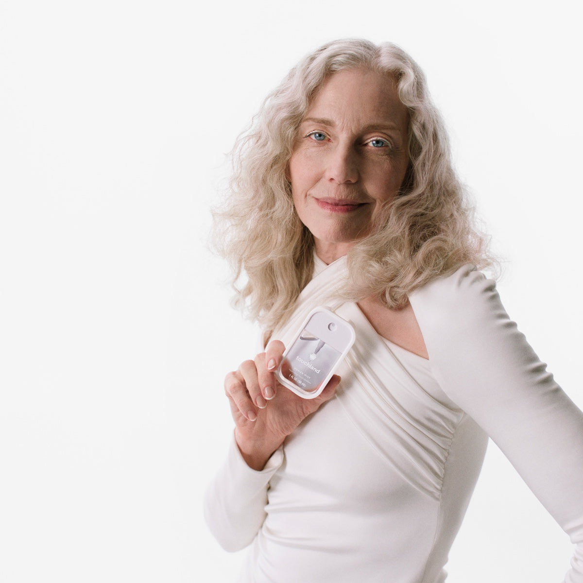 Woman holding Touchland hand sanitizer mist bottle, showcasing its sleek design and portability.