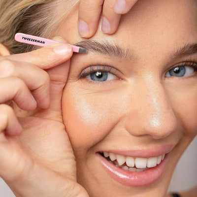 Close-up of woman shaping eyebrows with pink Tweezerman micro tweezer for precise grooming